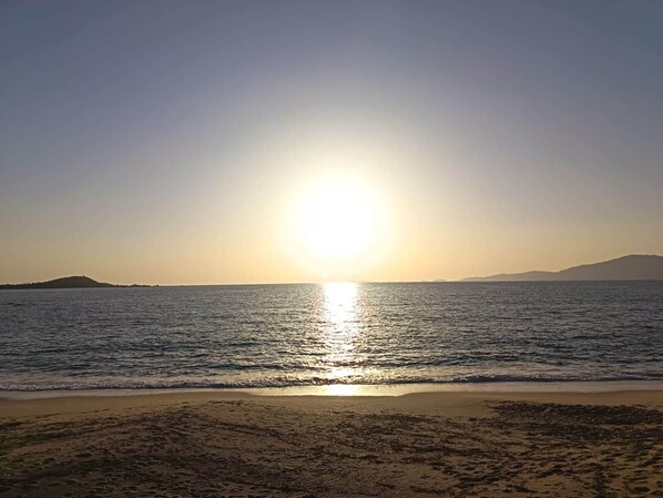 A beach with the sun reflecting on the water, distant hills, and a clear sky. - L'Écrin d'Olmo: Charming & spacious terrace in a peaceful setting (Pietrosella)