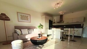 A modern living room with a sofa, a round coffee table, a floor lamp, and a kitchen area with bar stools. - L'Écrin d'Olmo: Charming & spacious terrace in a peaceful setting (Pietrosella)