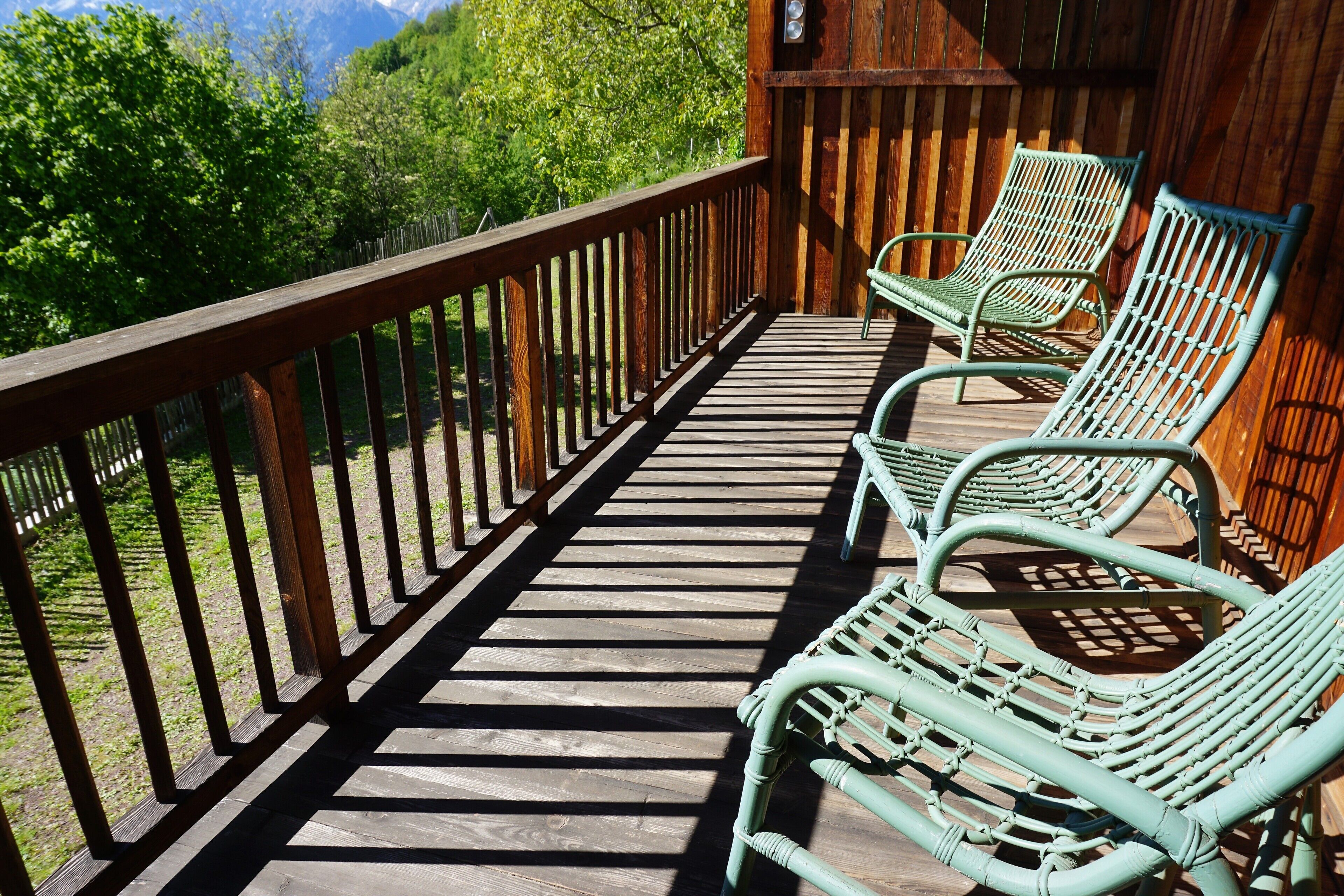 A wooden deck with a railing, two wicker chairs, and a view of greenery and mountains.