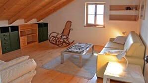 A cozy loft bedroom with a sloped ceiling, a rocking chair, a sofa, a small table, and a window.