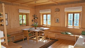 A wooden interior with a dining table, chairs, a bench, and windows.