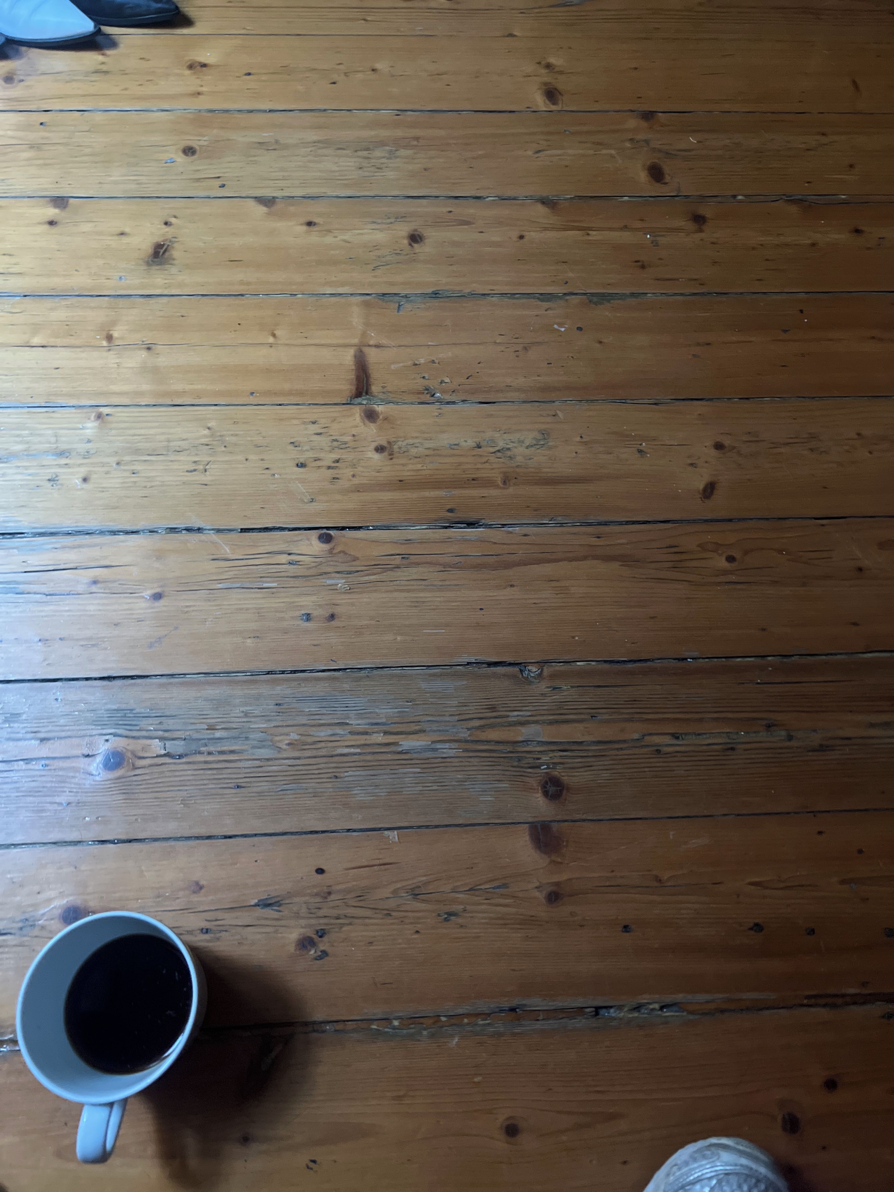 A wooden floor with a white mug and a clear glass.