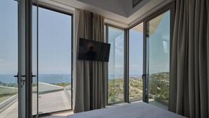Habitación de hotel con una cama grande, un televisor de pantalla plana montado en la pared y vistas panorámicas de la costa a través de ventanales de gran altura.