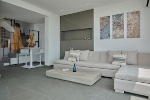 A modern living room with a sofa, coffee table, and abstract wall art. - Villa Anthos | Sea-view Villa with Pool & Jacuzzi (Βερβεροντα,)