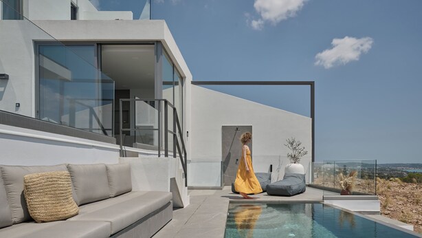 Un área de piscina exterior moderna con un sofá y una persona vestida de amarillo.