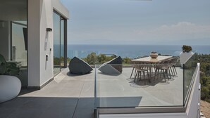 Un patio exterior moderno con barandilla de cristal, una mesa de comedor con sillas y vistas al mar.