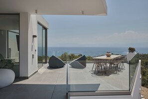 A modern outdoor patio with a glass balustrade, a dining table with chairs, and a view of the sea. - Villa Anthos | Sea-view Villa with Pool & Jacuzzi (Βερβεροντα,)