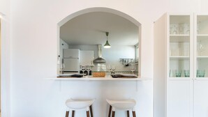 Eine Küche mit einem weißen Bogen, zwei weißen Barhocker und einem Schrank mit Gläsern.