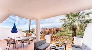 A balcony with a table, chairs, a sofa, and a blue umbrella. - Riviera Paradise | Terrace, Pools & Views REF902 (La Cala de Mijas)