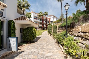 A stone pathway leading to a building with a white facade and red-tiled roof, surrounded by greenery and palm trees. - Riviera Paradise | Terrace, Pools & Views REF902 (La Cala de Mijas)