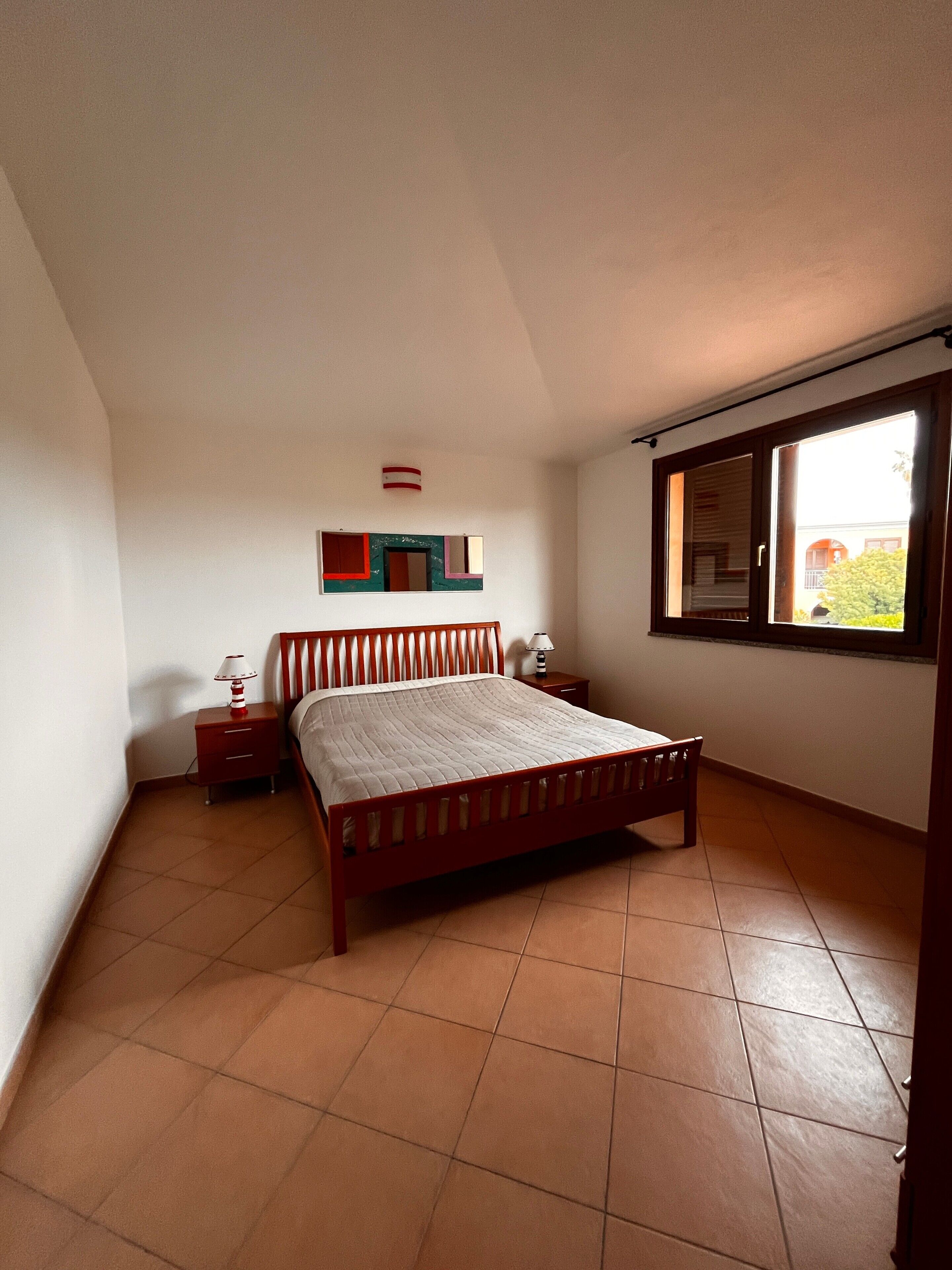 Une chambre à coucher comprenant un lit, une table de chevet, une lampe, une fenêtre et une étagère fixée au mur.