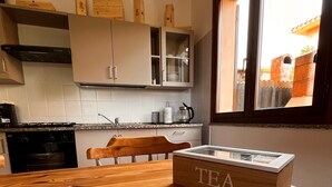 A kitchen with wooden cabinets, a stove, and a window with a view of a brick wall. - Holiday Home 'Rafael Villasimius House' with Private Garden, Wi-Fi and Air Conditioning (Villasimius)