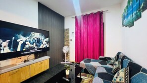 Un salon moderne avec un téléviseur à écran plat, un meuble en bois, un canapé noir et un rideau rouge.