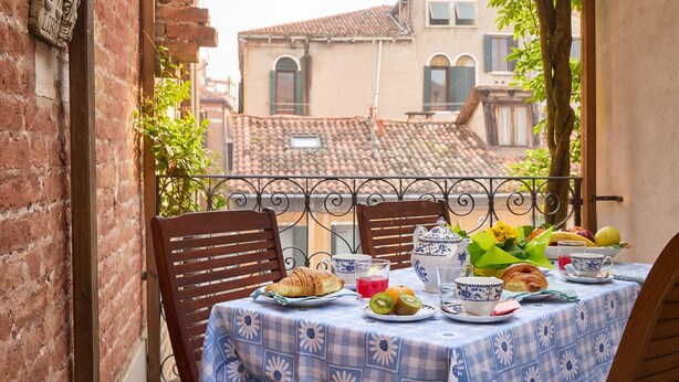 Un balcon avec une table préparée pour le petit-déjeuner, comprenant des croissants, des fruits et du thé.