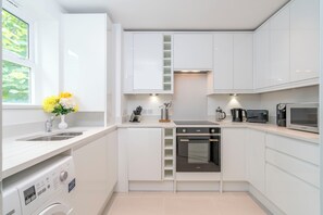 A modern kitchen with white cabinets, a built-in oven, a microwave, and a washing machine. - Urban Retreat in Vauxhall - 2BR Central Stay (London)