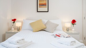 Cama bem arrumada com lençóis brancos, duas almofadas e um quadro emoldurado acima.