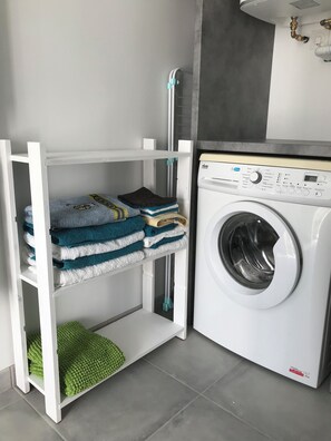 Ein kleiner Waschbereich mit Waschmaschine, Wäscheständer und Ablagefläche für gefaltete Handtücher.
