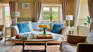 A cozy living room with a sofa, coffee table, and a view of greenery outside. - Rosedale Cottage (Brixham)