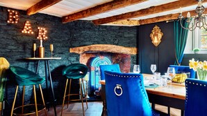 A rustic interior with exposed wooden beams, a stone wall, and a bar area with illuminated letters. - Rosedale Cottage (Brixham)