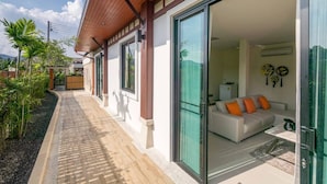A modern house with a covered patio, a white sofa with orange cushions, and a glass door leading to a living area. - Rawai VIP | Naiharn Beach | 3-bedroom Pool Villa (Rawai)