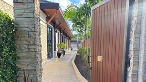 A pathway leading to a gated entrance with stone and brick walls, potted plants, and a clear sky. - Rawai VIP | Naiharn Beach | 3-bedroom Pool Villa (Rawai)