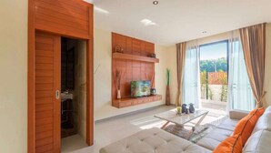 A modern living room with a sofa, TV, and a sliding door leading to a balcony. - Rawai VIP | Naiharn Beach | 3-bedroom Pool Villa (Rawai)