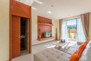 A modern living room with a sofa, TV, and a sliding door leading to a balcony. - Rawai VIP | Naiharn Beach | 3-bedroom Pool Villa (Rawai)