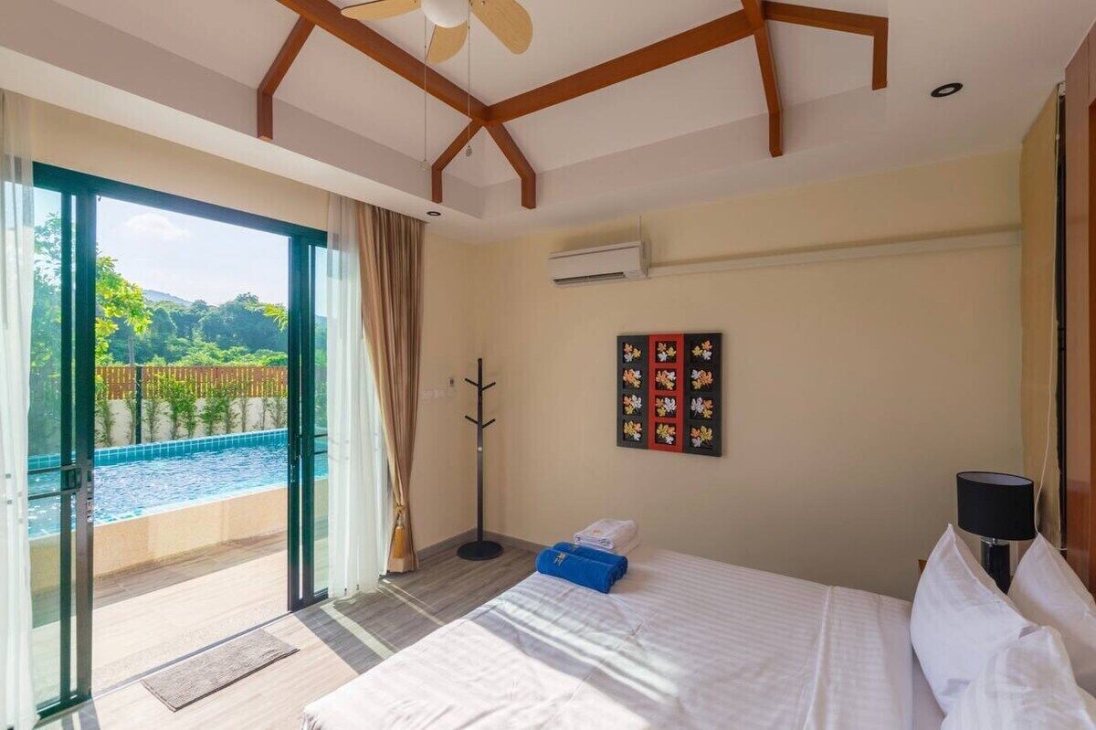 Quarto de hotel com cama, vista para uma piscina e ventoinha no teto.