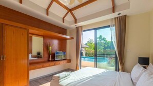 A bedroom with a large bed, a wooden wardrobe, a TV, and a view of a swimming pool. - Rawai VIP | Naiharn Beach | 3-bedroom Pool Villa (Rawai)
