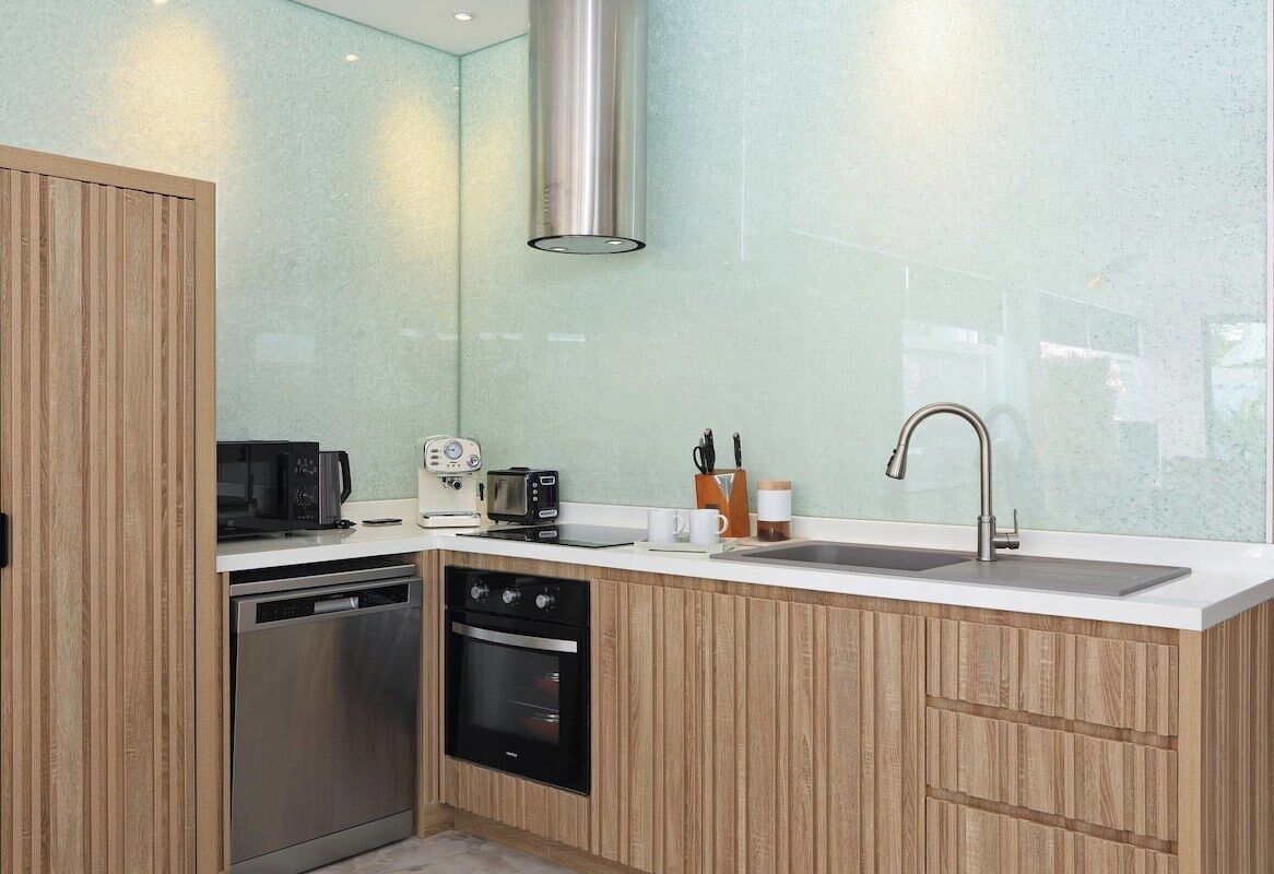 Una cocina moderna con armarios de madera, un lavamanos de acero inoxidable y electrodomésticos integrados, incluyendo lavavajillas y horno.