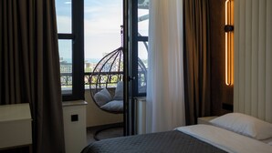 Quarto de hotel com cama, uma cadeira suspensa perto da janela e vista para a paisagem urbana.