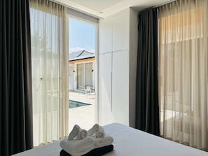 A hotel room with a bed, a view of a pool, and a sliding door leading to an outdoor area. - 4BR Pool Villa near Naiharn Garden View CapitalPro (Rawai)