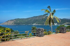 A coastal view with a palm tree, a stone structure, and a clear blue sky. - 4BR Pool Villa near Naiharn Garden View CapitalPro (Rawai)