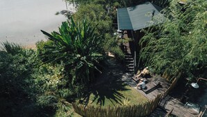 Una casa con techo verde, rodeada de vegetación densa y una masa de agua.