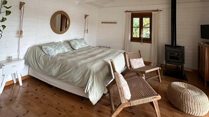 Un dormitorio con cama, dos sillas, una mesita, un espejo, una ventana y una chimenea.