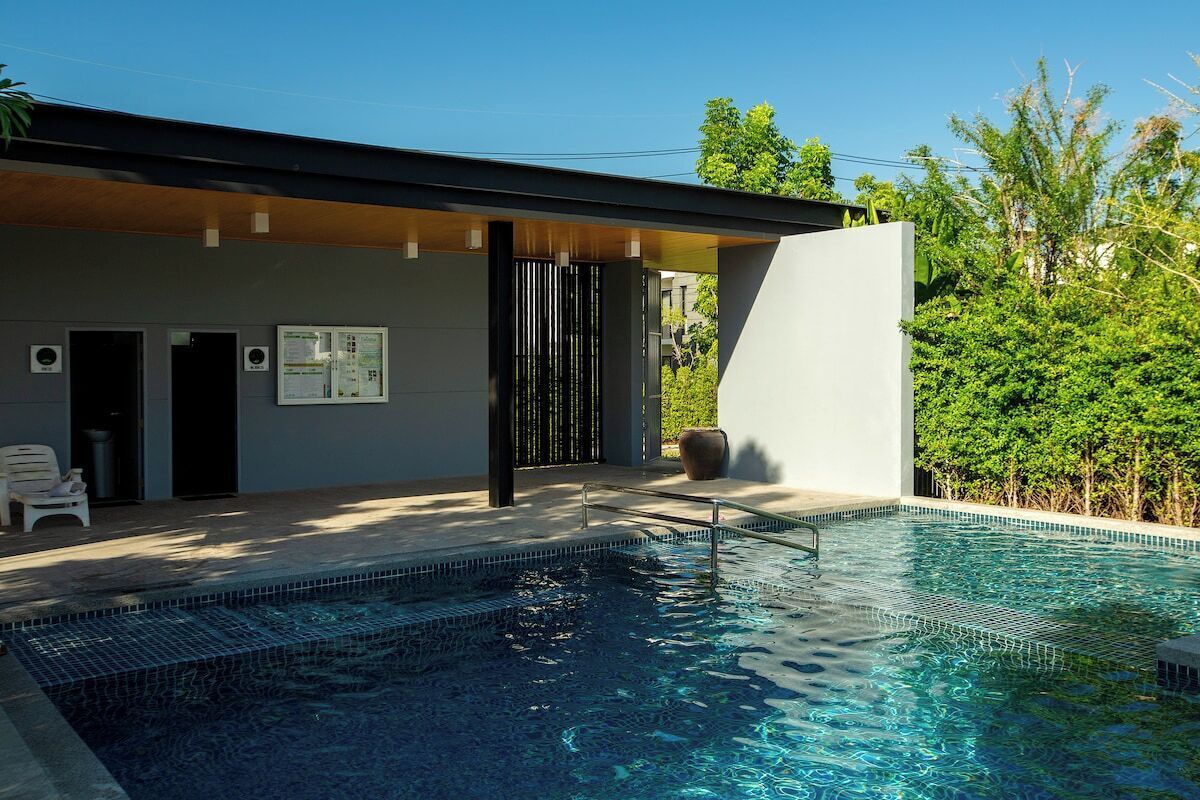 Un área de piscina moderna con una piscina cristalina, una zona de estar cubierta y un edificio de diseño minimalista.