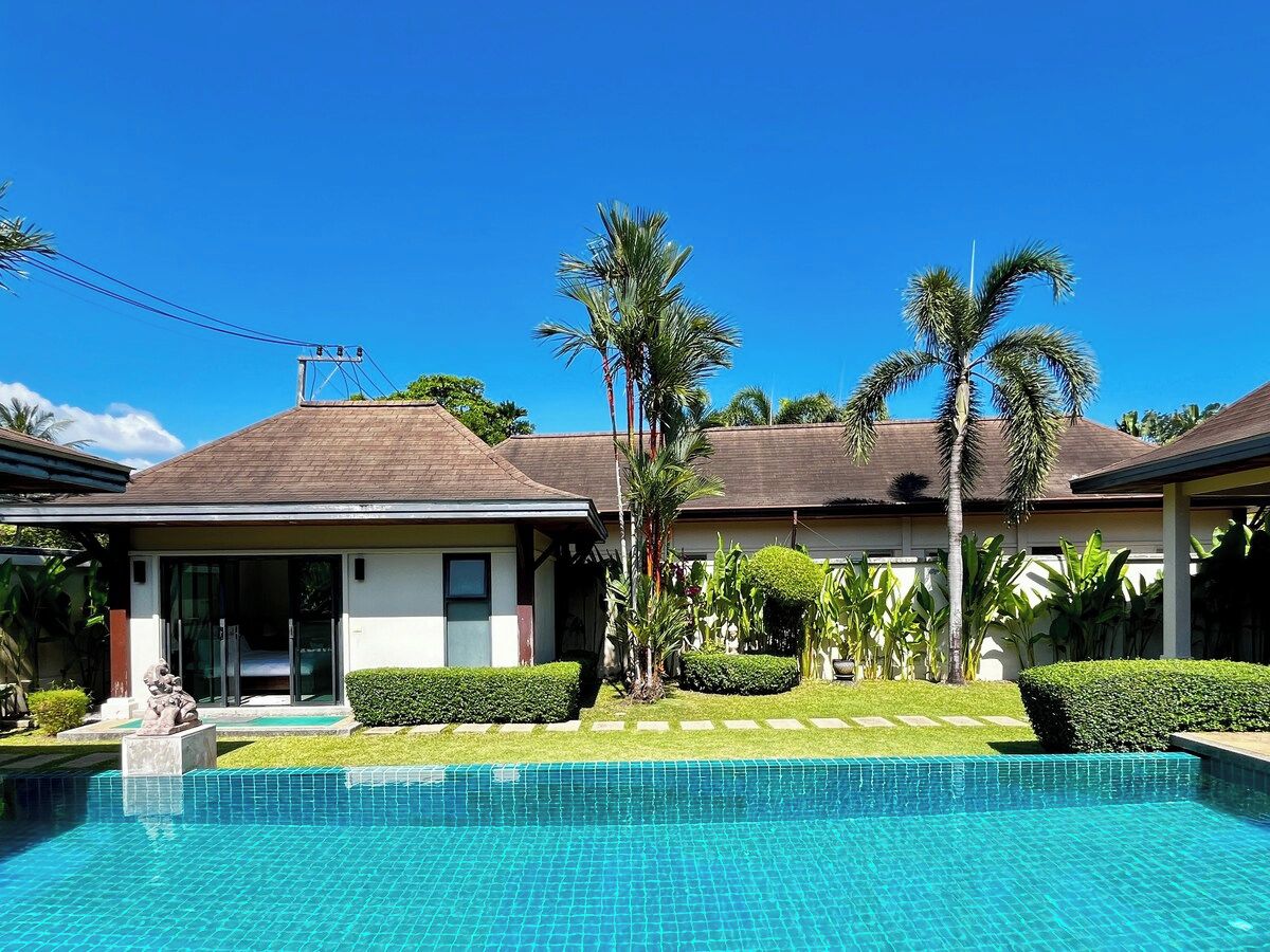 A house with a swimming pool, palm trees, and a clear blue sky.