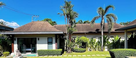 A house with a swimming pool, palm trees, and a clear blue sky.