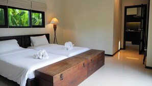 Ein Hotelzimmer mit einem großen Bett, einer hölzernen Bank, einer Nachttischlampe und Blick auf Grün hinter den Fenstern.