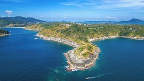 An aerial view of a coastal area with a prominent peninsula surrounded by water, a small island, and distant mountains. - 3BR Pool Villa Kokyang Rawai | Capital Pro (Rawai)