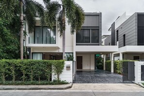 A modern multi-story residential building with a covered entrance and a black-tiled driveway. - Laguna Park | Bangtao Beach | 5-bedroom Rooftop Pool Villa (Tambon Choeng Thale)
