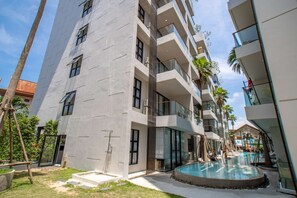 A modern multi-story building with a swimming pool, balconies, and a clear sky. - 2BR Apartment · Palmyrah Surin · Surin | CapitalPro (Tambon Choeng Thale)