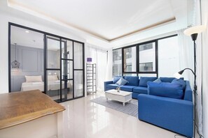 Een moderne woonkamer met een blauwe bank, een houten salontafel en een glazen deur die naar een slaapkamer leidt.