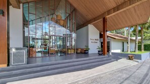 Ein modernes Gebäude mit Glasfassade, einem überdachten Eingangsbereich mit Stufen und Außenbestuhlung.