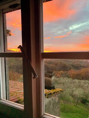 A window with a view of a sunset over a landscape with trees and a building. - Apartment in farmhouse, nestled in olive grove, 15 minutes from Lucca (Capannori)