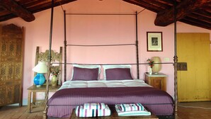 Una stanza con un letto a baldacchino, soffitto in legno, parete rosa e una porta di legno.