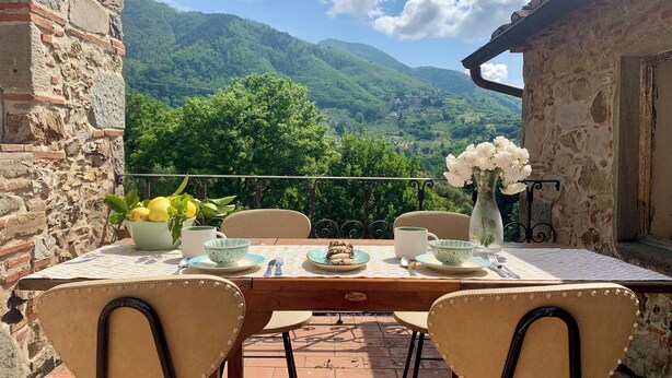 Un tavolo apparecchiato all'aperto con vista sulle montagne, circondato da mura in pietra.