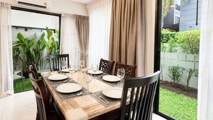 A dining area with a table set for four, chairs, and a view of a garden through a glass door. - 3BR Townhouse with Jacuzzi & Lake View |CapitalPro (Tambon Choeng Thale)