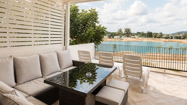 A covered outdoor seating area with a glass-top table, white cushioned sofa, and wicker chairs. - 3BR Townhouse with Jacuzzi & Lake View |CapitalPro (Tambon Choeng Thale)