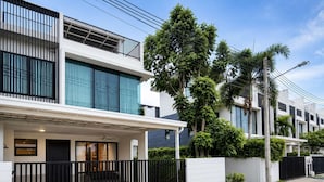 A modern residential building with a covered porch, a black fence, and a well-maintained garden. - 3BR Townhouse with Jacuzzi & Lake View |CapitalPro (Tambon Choeng Thale)